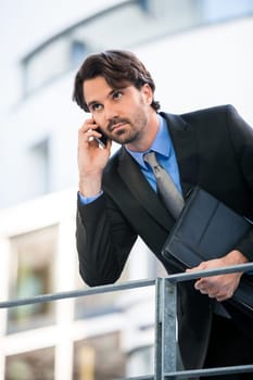 Young trendy successful businessman with mobile phone smartphone cheerful lyrane in front of an outdoor business building