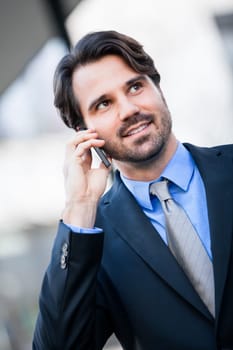 Young trendy successful businessman with mobile phone smartphone cheerful lyrane in front of an outdoor business building