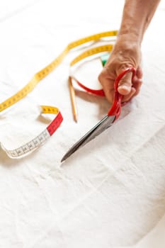 Hands with measuring tape scissors and pen when measuring fabric for the tailoring textile as a close-up