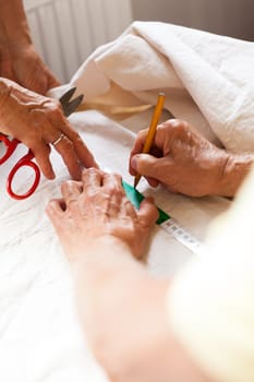 Hands with measuring tape scissors and pen when measuring fabric for the tailoring textile as a close-up