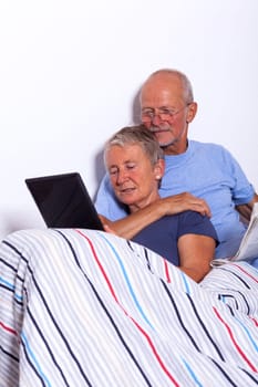Senior couple with husband and wife lie in bed in the morning evening together with a tablet and a newspaper