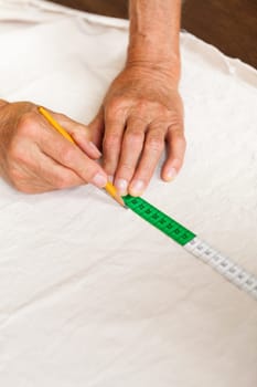 Hands with measuring tape scissors and pen when measuring fabric for the tailoring textile as a close-up