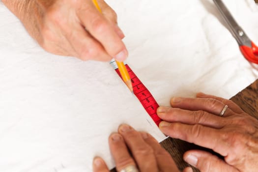 Hands with measuring tape scissors and pen when measuring fabric for the tailoring textile as a close-up