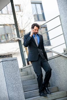 Young trendy successful businessman with mobile phone smartphone cheerful lyrane in front of an outdoor business building
