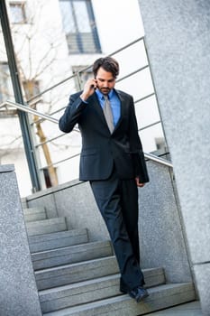 Young trendy successful businessman with mobile phone smartphone cheerful lyrane in front of an outdoor business building