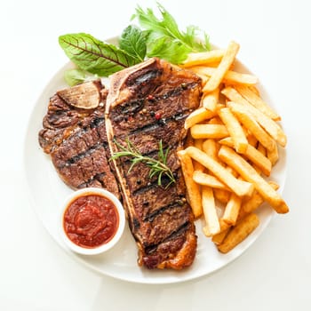Grilled t-bone or porterhouse steak seasoned with rosemary and served with golden French fries, fresh leafy herb salad and a tomato dip, high angle view on white