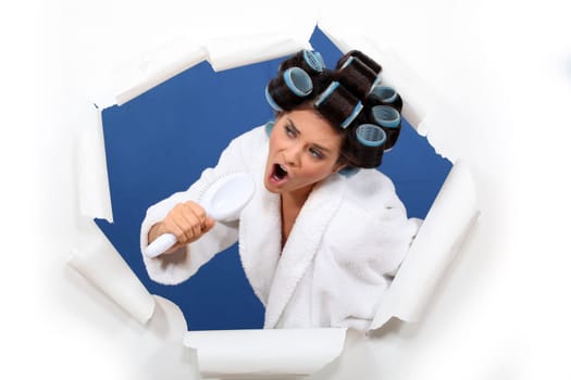 Woman wearing hair rollers, singing into brush