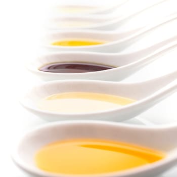 Assorted oils and vinegar in white ceramic spoons used as ingredients in cooking or as a salad dressing, close up view in a receding row