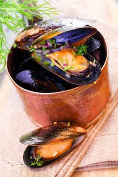 Delicious freshly boiled marine mussels in a copper saucepan with their shells open garnished with dill for a gourmet seafood starter, high angle closeup view