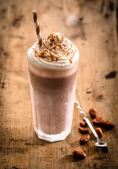 Glass of thick creamy coffee milkshake, frappe or iced coffee with a topping of ice cream and drizzled syrup on an old wooden table, high angle view
