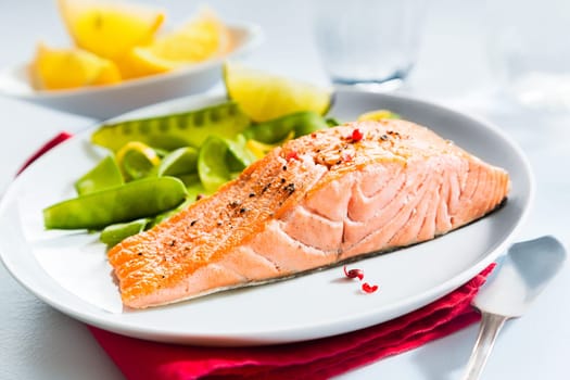 Gourmet seafood meal of grilled salmon steak served with fresh green mangetout peas and lemon wedges for flavoring