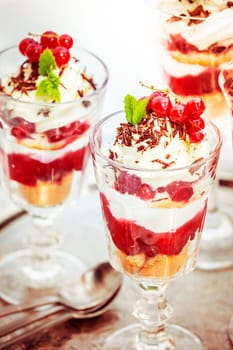 Tall glasses of colorful layered redcurrant and ice cream parfait topped with bunches of fresh fruit sprinkled with chocolate flakes for a delicious gourmet dessert