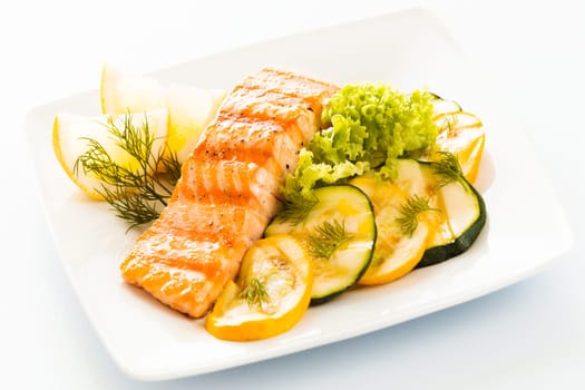 Salmon steak with sliced zucchini and courgette, lettuce and lemon garnished with fresh dill for a tasty seafood platter or appetizer