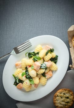 Traditional Italian cuisine with a plate of gnocchi pasta, or dumplings, made with semolina and served with basil and grilled salmon cubes, view from above on grey with copyspace