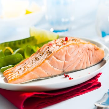 Healthy gourmet pink salmon steak rich in omega-3 served with fresh green mangetout peas and lemon, close up showing the texture of the fish