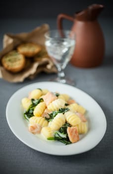 Italian gnocchi pasts served with salmon and basil on an oval platter with a glass of white wine and toasted herb buns