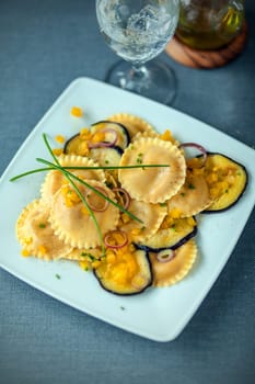Delicious Italian vegetarian cuisine with round girasole ravioli and aubergine or eggplant topped with chives and served with a glass of wine