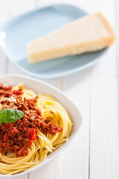 Bowl of delicious Italian spaghetti Bolognese topped with a rich meat and tomato sauce and sprinkled with grated parmesan cheese with a wedge behind