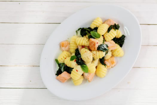 Overhead view of a plate of sauteed Italian gnocchi with salmon and basil on a rustic wooden white picnic table for a healthy lunchtime snack, with copyspace