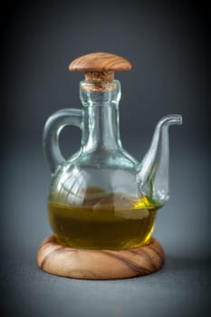 Transparent glass decanter with a wooden stopper half filled with healthy olive oil to use as a dressing for salads or cooking ingredient, on grey