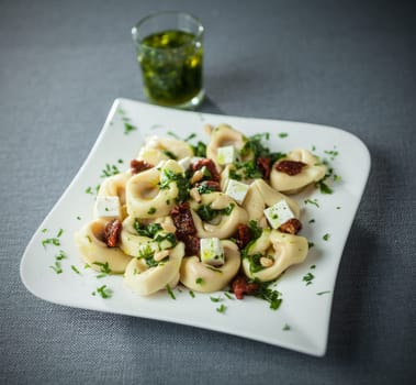 Italian tortellini pasta with feta cheese and basil and pine nut pesto drizzled with virgin olive oil on a modern stylish plate