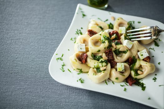 Serving of feta cheese, basil and pine nut pesto with Italian tortellini pasta on a modern curved white plate over a grey cloth with copyspace