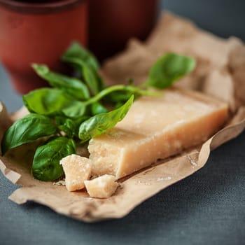 Wedge of hardy crumbly Italian Parmigiano-Reggiano, or Parmesan, cheese with fresh basil leaves on a crumpled brown paper wrapper