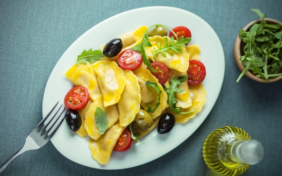 Italian ravioli salad with fresh rocket or arugula, cherry tomatoes and olives drizzled with virgin olive oil, view from above