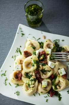 View from above of a stylish white plate with tortellini pasta, basil pesto and feta cheese sprinkled with fresh chopped herbs