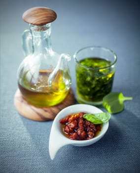 Decanter of virgin olive oil, pesto and a bowl of spicy piquant tomato dip viewed high angle on a grey tablecloth with vignetting and copyspace