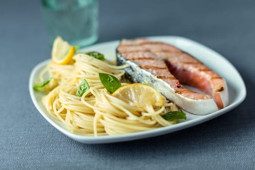 Italian linguine pasta topped with fresh basil leaves served with a gourmet grilled salmon steak for a delicious seafood dinner