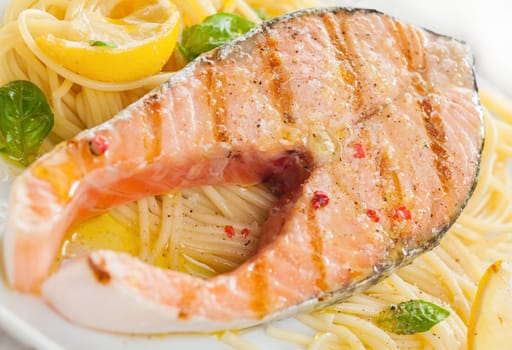 Grilled salmon cutlet with linguine pasta, basil and lemon for a gourmet Italian seafood dinner, close up view and texture