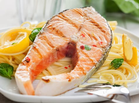 Gourmet grilled salmon steak or fillet on a bed of Italian linguine pasta with fresh basil and lemon, close up view