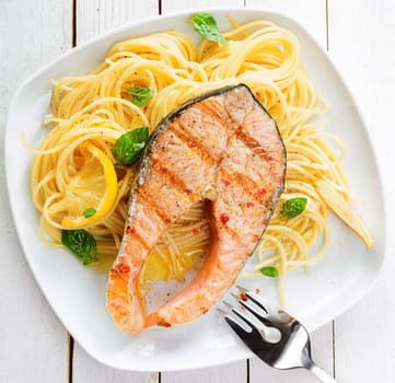 Healthy grilled salmon steak rich in omega-3 fatty acids served on linguine pasta topped with fresh basil , overhead view