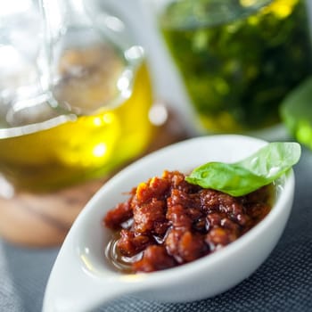 Savory accompaniments served in a restaurant with a bowl of piquant chutney or spicy dip, virgin olive oil, and fresh basil pesto, close up view