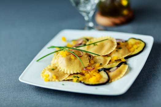 Vegetarian Italian ravioli pasta with grilled or roasted slices of eggplant or aubergine served on a modern square plate topped with fresh chives