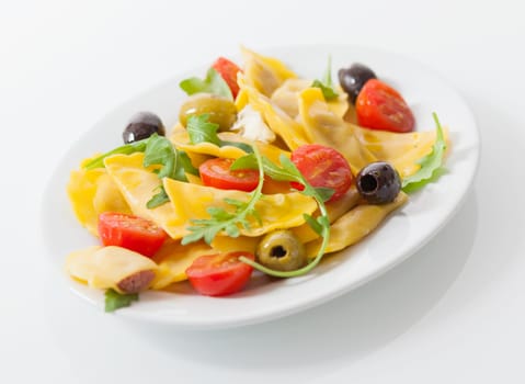 Delicious savory Italian ravioli salad with stuffed ravioli pasta, fresh rock and cherry tomatoes and a variety of olives , close up low angle view on a plate