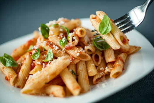 Penne pasta with a spicy sauce, basil and grated parmesan cheese with a forkful of pasta suspended above the plate with focus to the fork