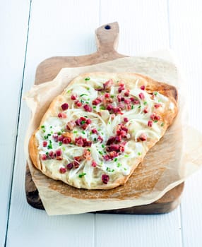 Tarte Flambee, a traditional French tart from the Alasace region, with a thing pastry base, creme fraiche or cheese, lardons - cubed smoked bacon, onions and fresh herbs served on a wooden board