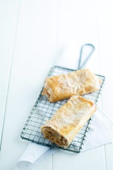 Fresh German apfelstrudel or apple strudel with delicious light puff pastry enclosing an apple filling dusted with powdered sugar served on a wire rack in a country restaurant, high key with copyspace