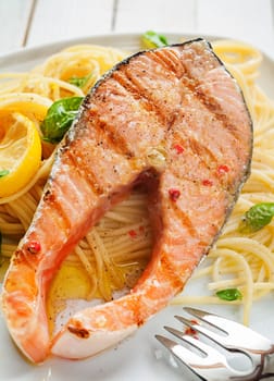 Seafood dinner of a gourmet grilled salmon cutlet steak on Italian linguine pasta seasoned with fresh basil and garnished with lemon