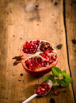Halved fresh pomegranate with seeds in a teaspoon rich in vitamins and used in ayurvedic medicine on a rustic wooden table with copyspace