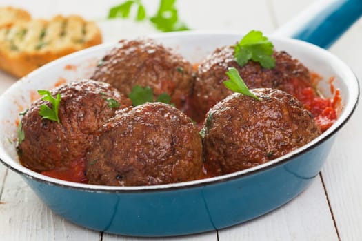 Frying pan with five savory Italian meatballs in spicy tomato sauce garnished with fresh basil, closeup low angle view