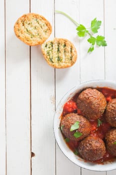 Savory beef meatballs in a spicy tomato sauce with fresh herbs served in a saucepan with crisp golden grilled herb bread and fresh parsley on a white wooden table, view from above