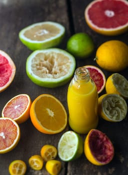 Preparing fresh citrus juice in a rustic kitchen with a bottle of orange juice blend surrounded by halved oranges, grapefruit, blood orange , lime and lemon, some of which have been squeezed