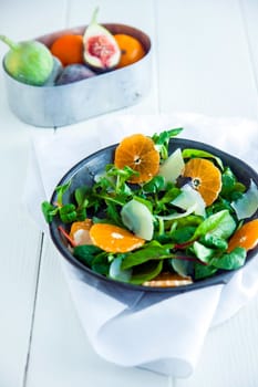 Healthy mache salad with sliced oranges and parmesan cheese served in a bowl on a white wooden table with a bowl of fresh fruit in the background