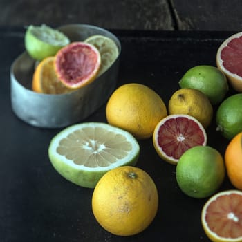 Juicing a selection of fresh citrus fruit with grapefruit, oranges, limes and lemons and a metal container with squeezed skin remnants