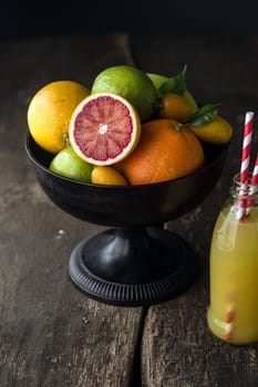 Bowl of assorted fresh citrus fruit with a halved blood orange with its distinctive red pulp in the foreground with a bottle of freshly squeezed orange juice