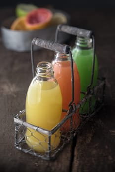 Glass bottles of assorted fresh fruit juice in an old metal and wire rack in a rustic kitchen with orange, grapefruit and lemon and lime blends