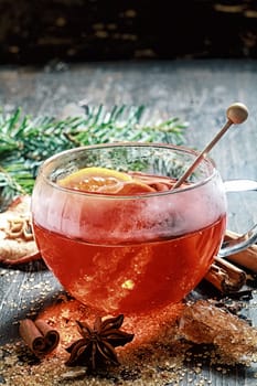 Hot cup of spiced hot tea or gluhwein with a crystallized sugar stirrer and citrus fruit surrounded by dried cinammon , star anise and caramelised sugar on a rustic Christmas backdrop with copyspace